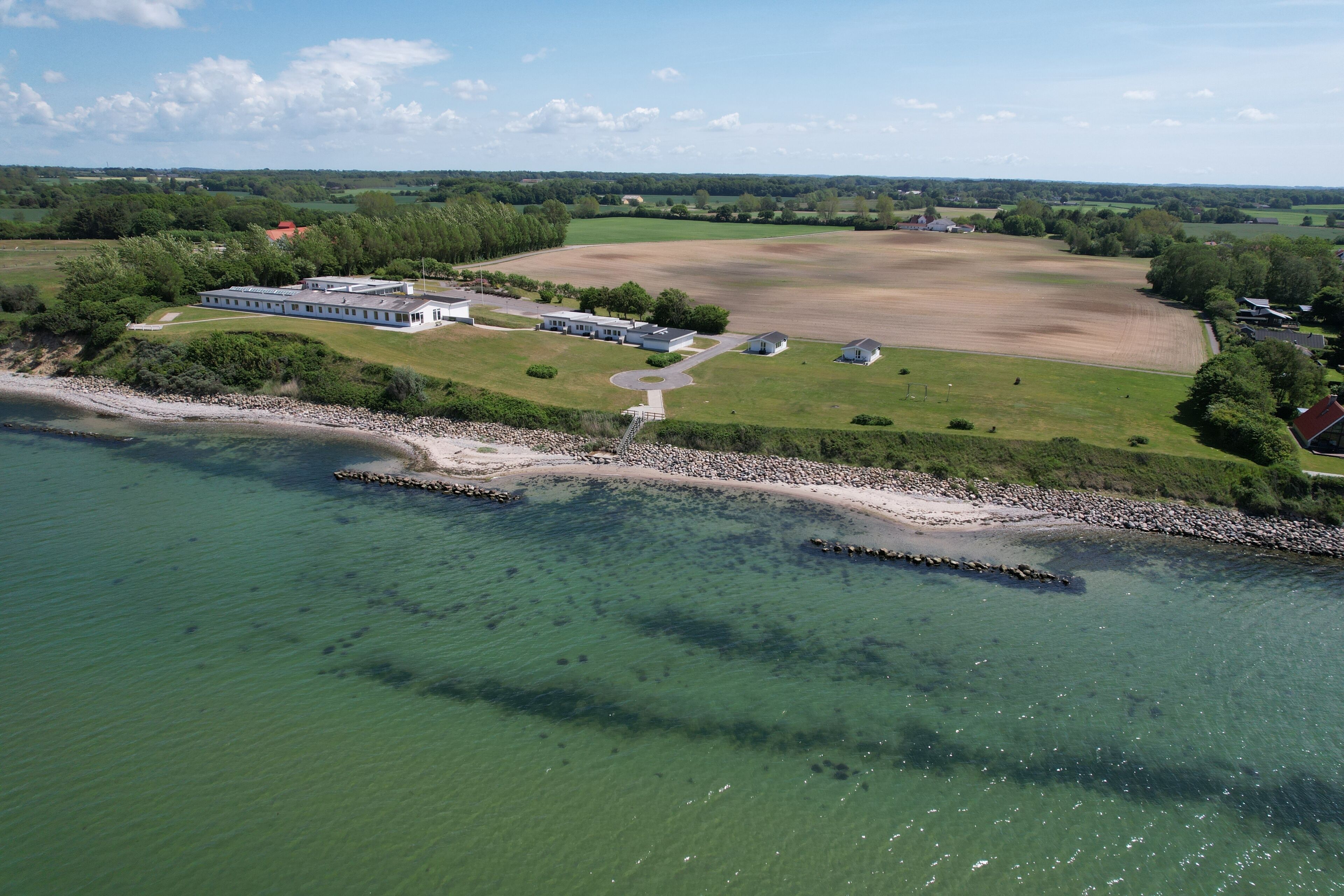 An aerial view of a coastal property with a large building, a dock, and surrounding fields.