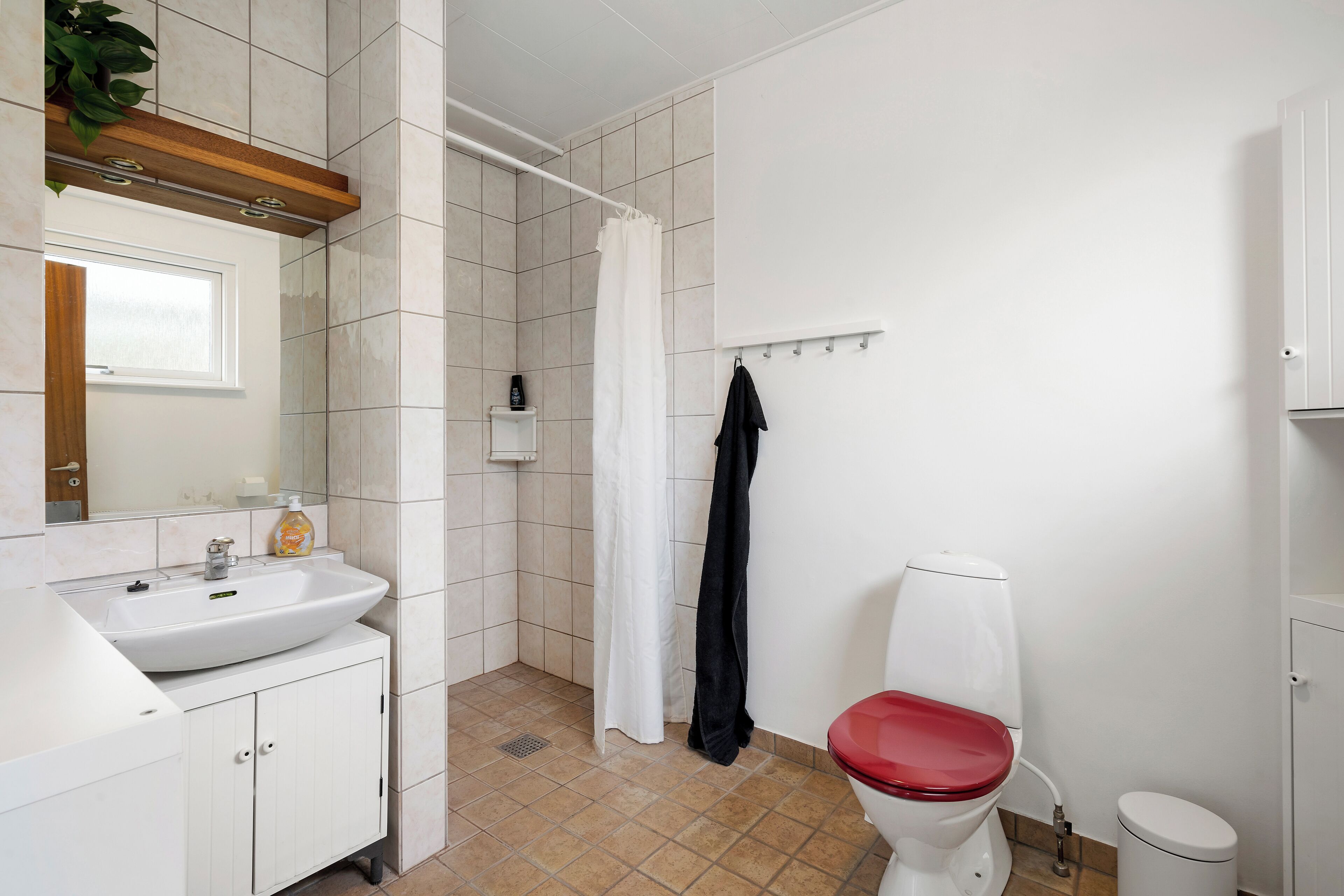 A bathroom with a white sink, a red toilet, a shower curtain, and a towel rack.