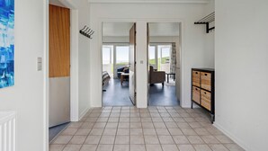 Un couloir mène à un espace de vie comprenant un canapé, une table et une vue sur l’extérieur.