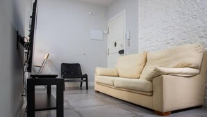 A living room with a beige sofa, a black chair, a small table, and a white door. - Retiro VI (Madrid)