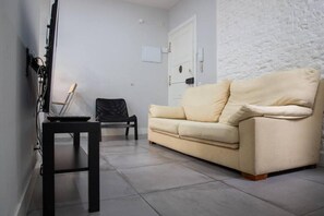 A living room with a beige sofa, a black chair, a small table, and a white door. - Retiro VI (Madrid)