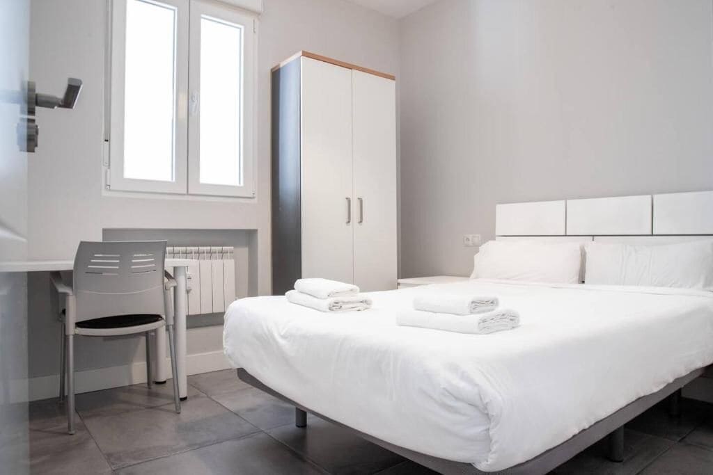 A modern hotel room with a large bed, a wardrobe, a desk, and a chair.
