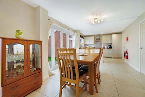 A dining area with a wooden table and chairs, a glass cabinet with decorative items, and a kitchen in the background.