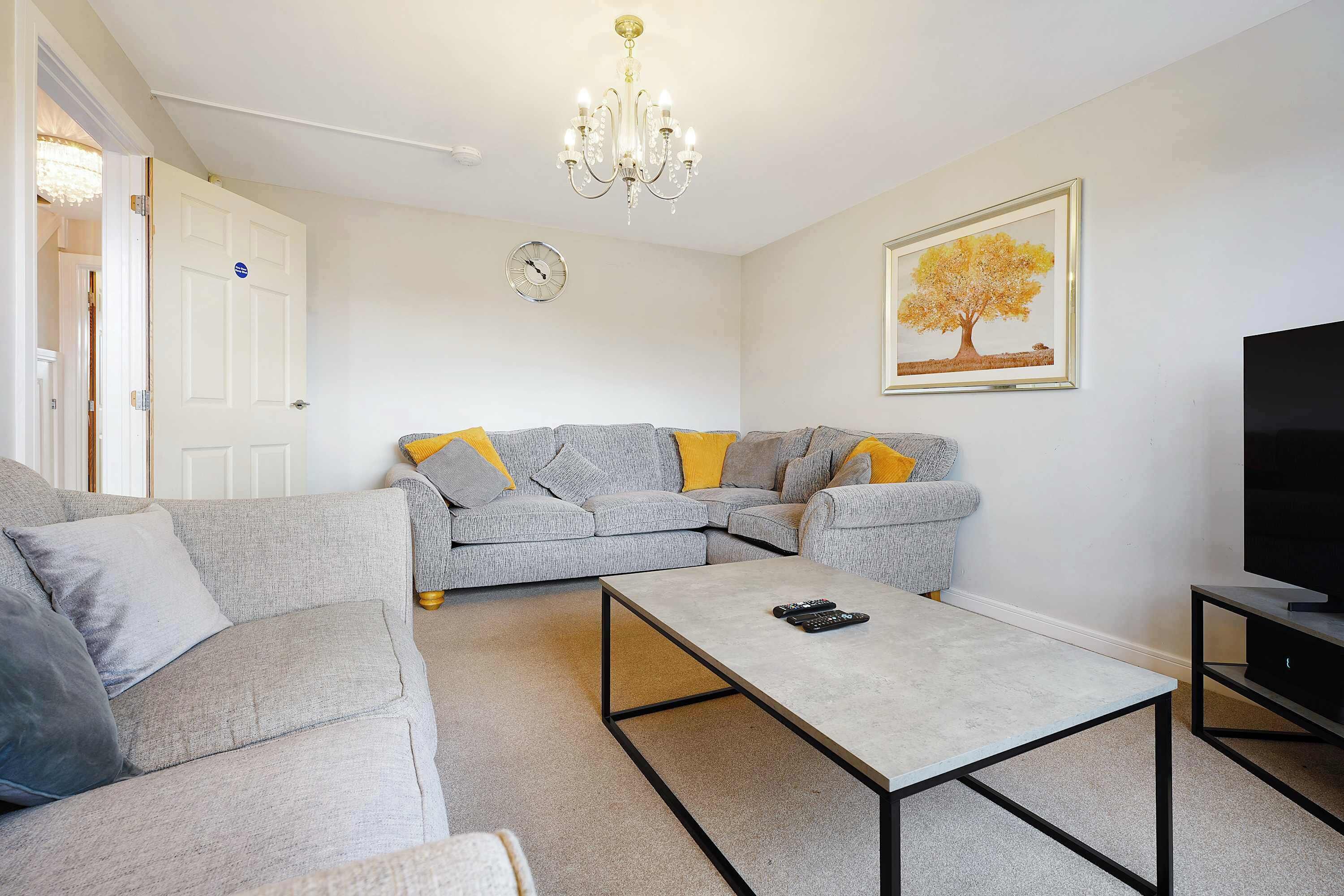 Ein Wohnzimmer mit grauem Sofa, Couchtisch, einer Chandelierleuchtre, einer Uhr und einem gerahmten Bild an der Wand.