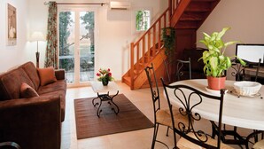 A living room with a sofa, a dining table with chairs, a staircase, and a potted plant.