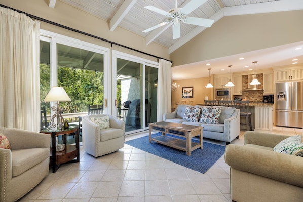 A spacious living area with a large sliding glass door leading to a balcony, a kitchen with modern appliances, and a ceiling fan.