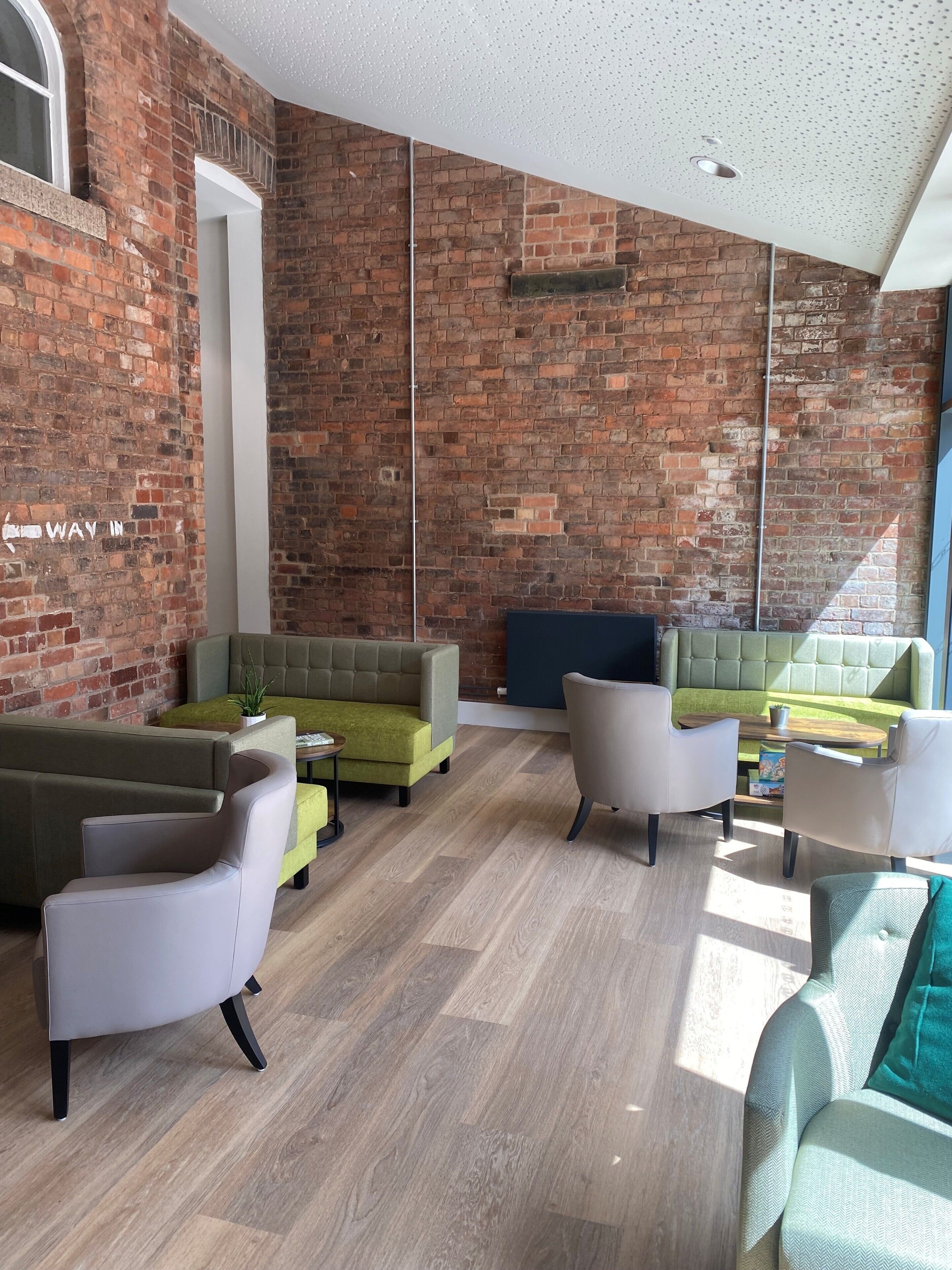 Un salon moderne avec des murs en briques, des canapés verts et des fauteuils blancs.