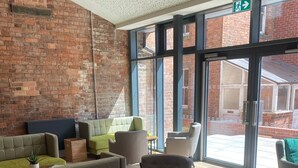 Un vestíbulo con pared de ladrillo, ventanas amplias y varias zonas de estar con sofás y sillones.