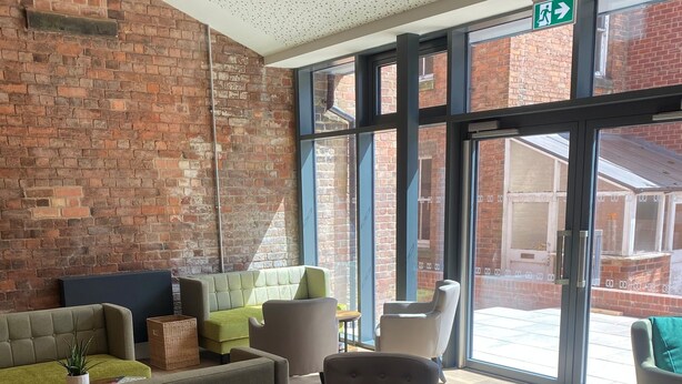 Un vestíbulo con pared de ladrillo, ventanas amplias y varias zonas de estar con sofás y sillones.