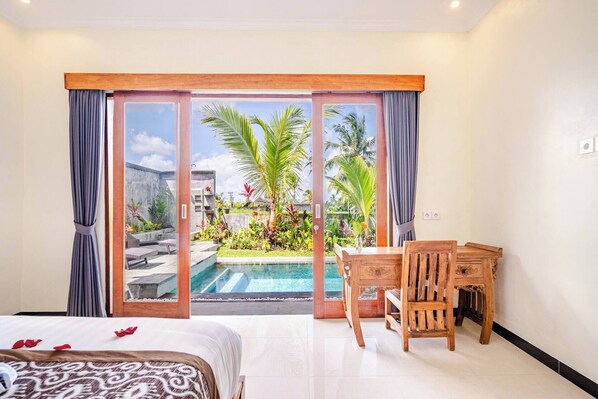 Ein Hotelzimmer mit Bett, Schreibtisch und Blick auf ein Schwimmbad und Palmen.