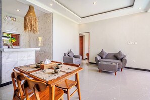 Ein modernes Wohnzimmer mit Marmorboden, einem Essbereich mit Holztisch und Stühlen, einem grauen Sofa und einer hängenden Leuchte.
