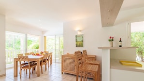 A dining area with wooden furniture, a kitchen counter, and a large window with a view of greenery. - Superior Villa Escape in Lacanau (Lacanau)