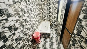 A bathroom with a bathtub, a toilet, and a shower area. - Hotel Grand Riva (Rajkot)