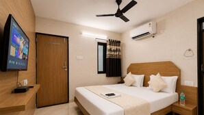 A hotel room with a bed, a TV, a ceiling fan, an air conditioner, and a window with curtains. - Hotel Grand Riva (Rajkot)