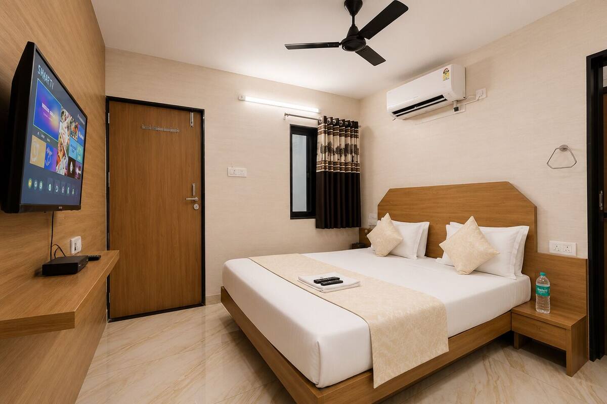 Habitación de hotel con cama, televisor, ventilador de techo, aire acondicionado y ventana con cortinas.