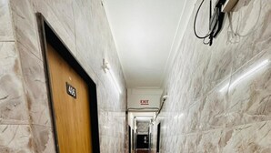 A marble-floored hallway with an exit sign, a door labeled '406,' and a wall-mounted electrical outlet. - Hotel Grand Riva (Rajkot)