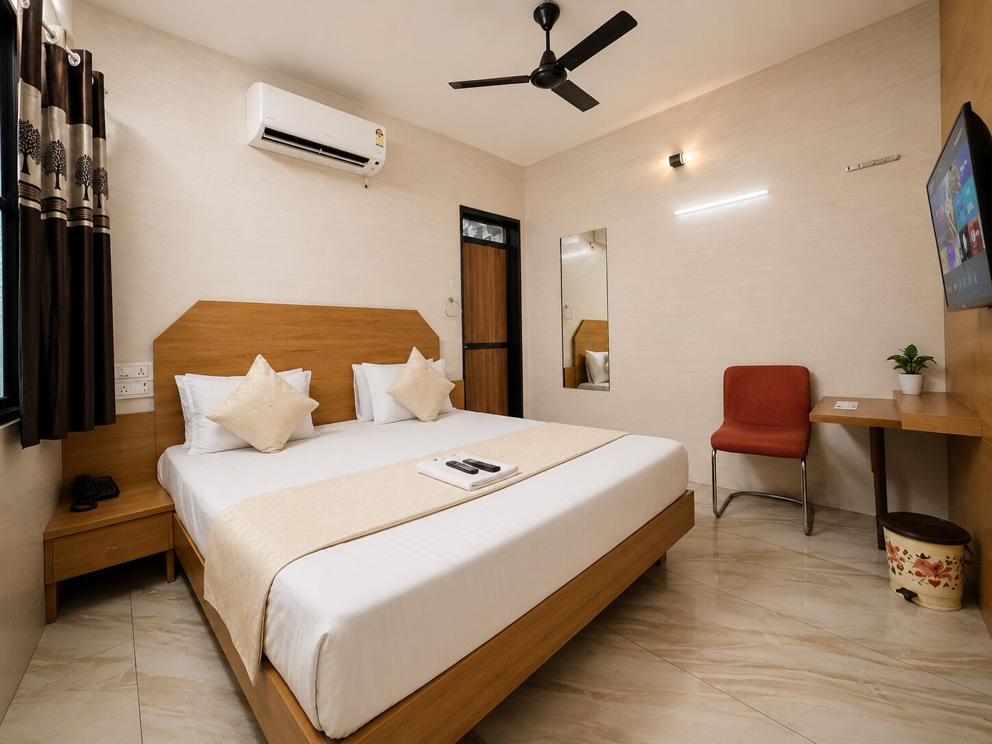 A hotel room with a bed, bedside table, chair, desk, air conditioning unit, ceiling fan, and a mirror.