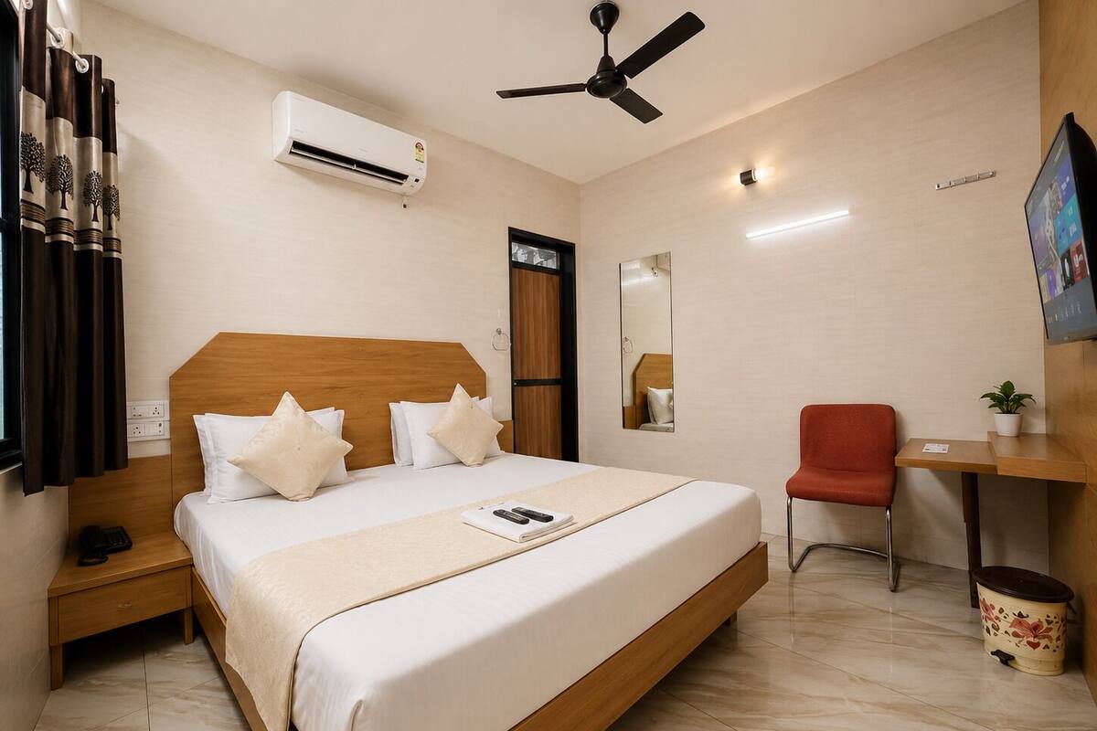 Habitación de hotel con cama, mesita de noche, silla, escritorio, aire acondicionado y espejo.