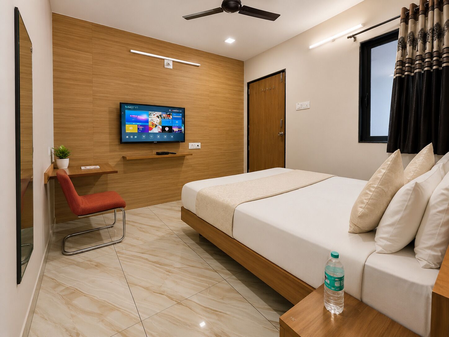 A modern hotel room with a bed, a TV, a red chair, a wooden desk, and a water bottle.