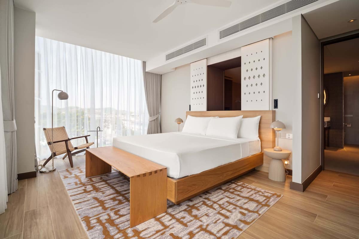 Une chambre d’hôtel moderne avec un grand lit, une table de chevet, une chaise et une vue sur la ville.