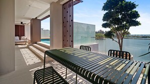 A modern outdoor seating area with a table and chairs, a glass balustrade, and a view of a lake. - Angsana Oceanview Residences Building 2 in Laguna by Banyan Living (Choeng Thale)