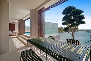 A modern outdoor seating area with a table and chairs, a glass balustrade, and a view of a lake. - Angsana Oceanview Residences Building 2 in Laguna by Banyan Living (Choeng Thale)