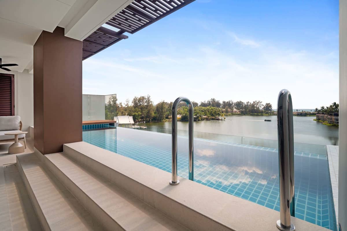 A modern infinity pool with a clear view of a lake and trees, a covered seating area, and a staircase leading to the pool.