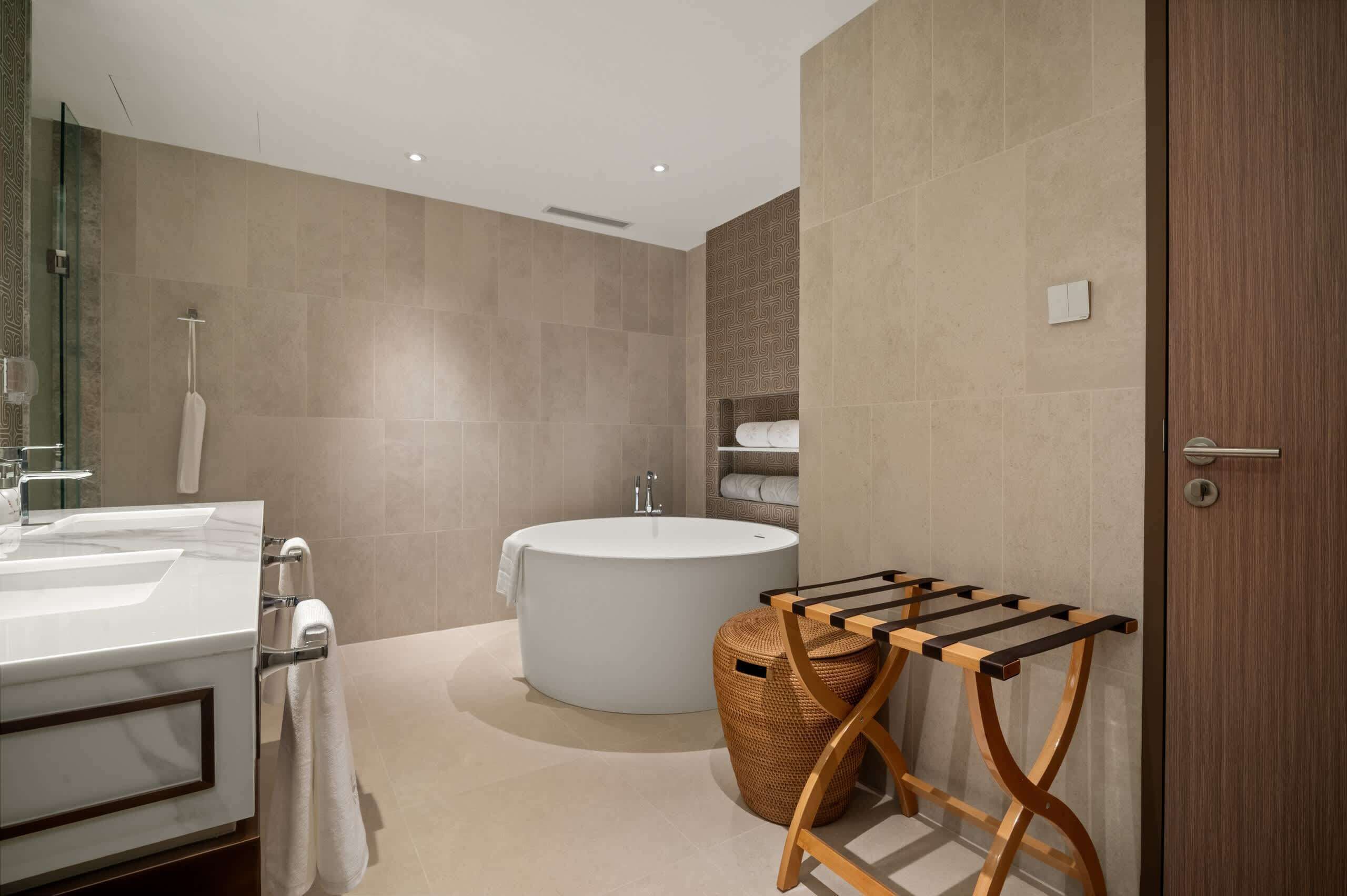 A modern bathroom with a large bathtub, a vanity with a mirror, and a wooden towel rack.