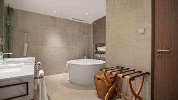 A modern bathroom with a large bathtub, a vanity with a mirror, and a wooden towel rack.