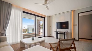 A modern hotel room with a large bed, a seating area with a table, a television, and a balcony with a view. - Angsana Oceanview Residences Building 2 in Laguna by Banyan Living (Choeng Thale)