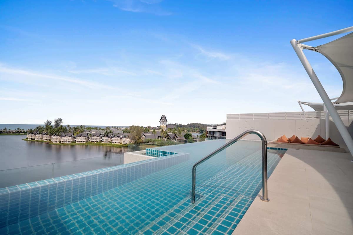 A swimming pool with a view of a resort area, including a building with a clock tower and a body of water.