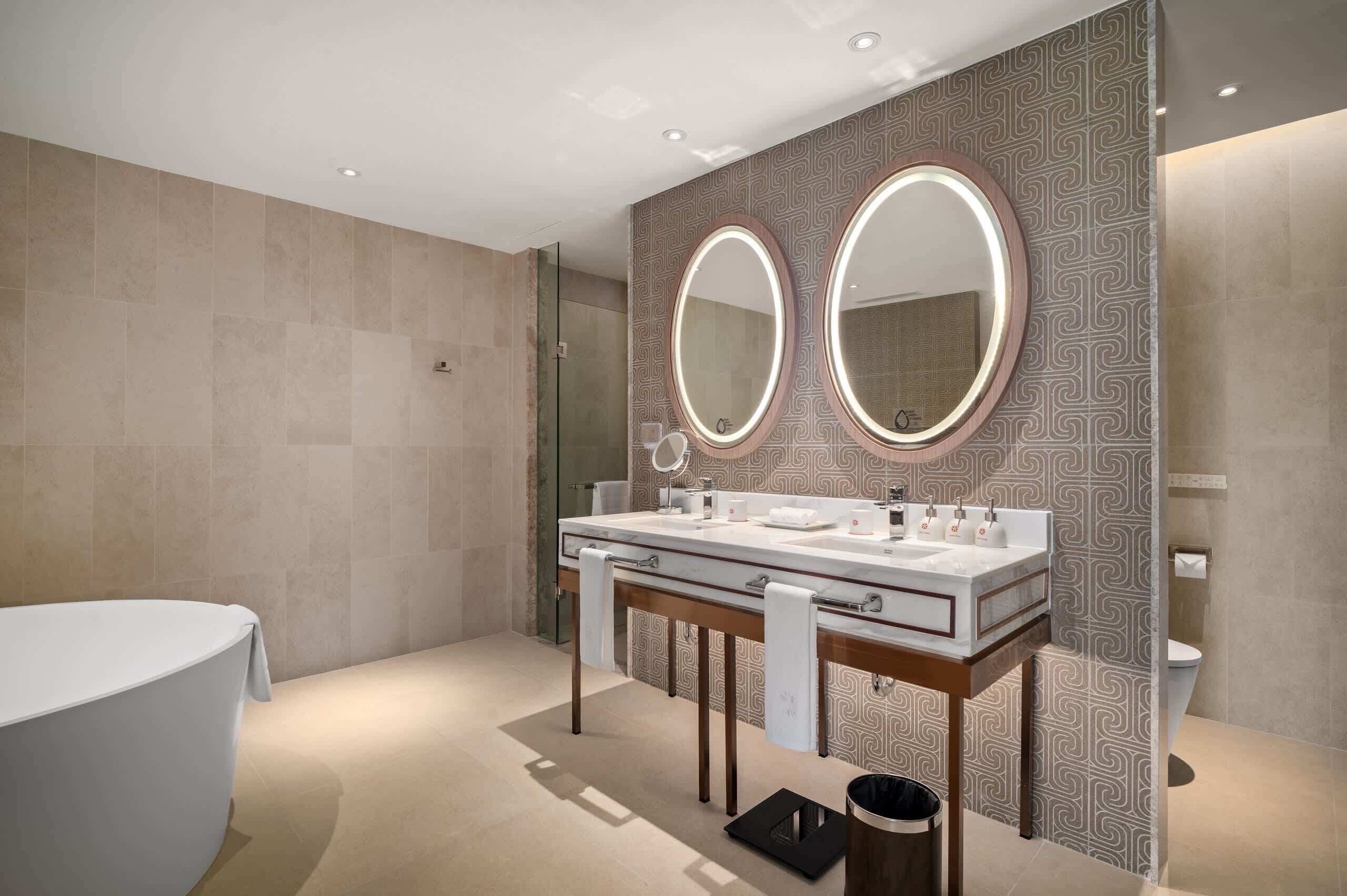 Un bagno moderno con doppio lavabo, due ampi specchi, una vasca e un water.