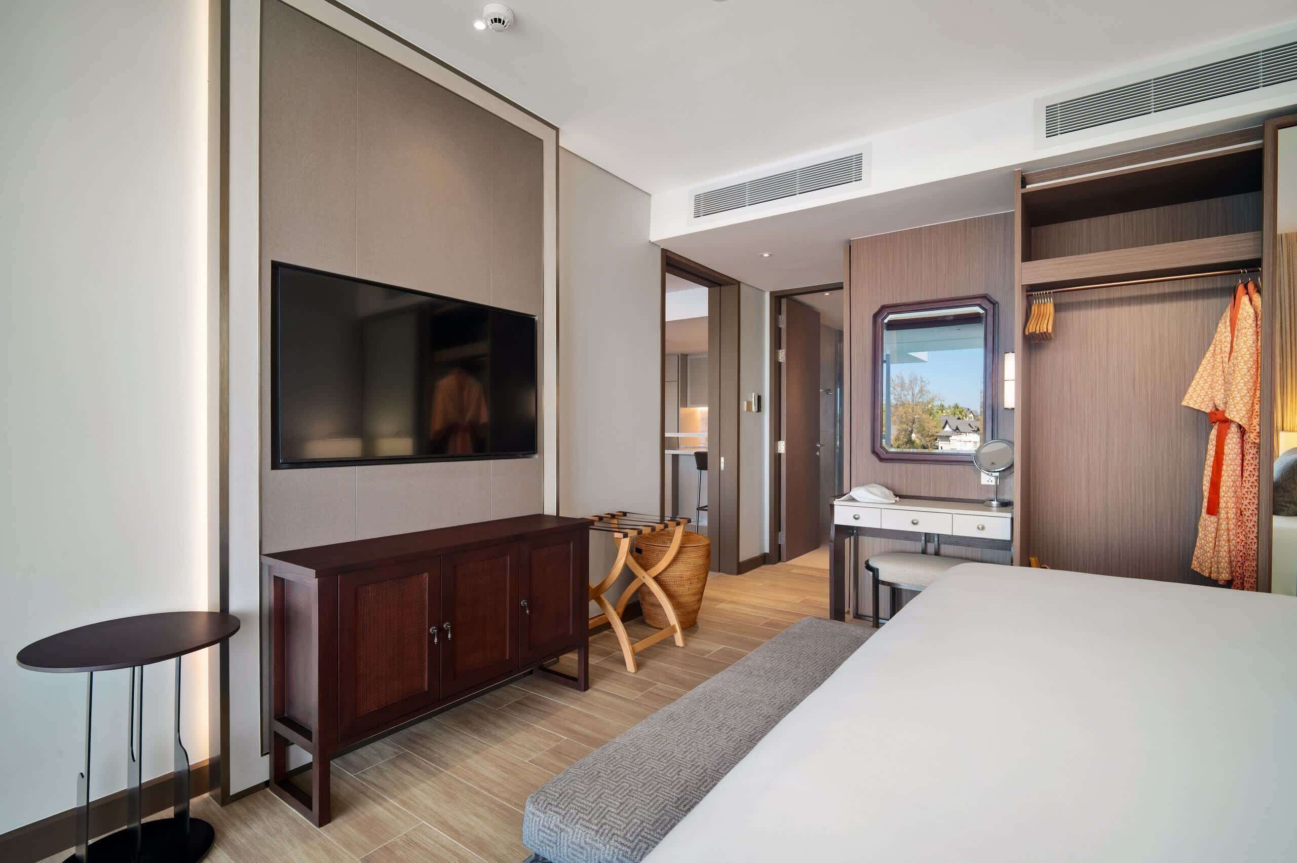 A modern hotel room with a bed, a desk, a TV, and a wardrobe.