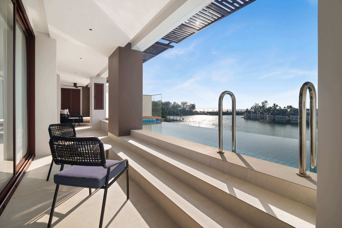 A balcony with a view of a body of water, steps leading to a pool, and a chair.