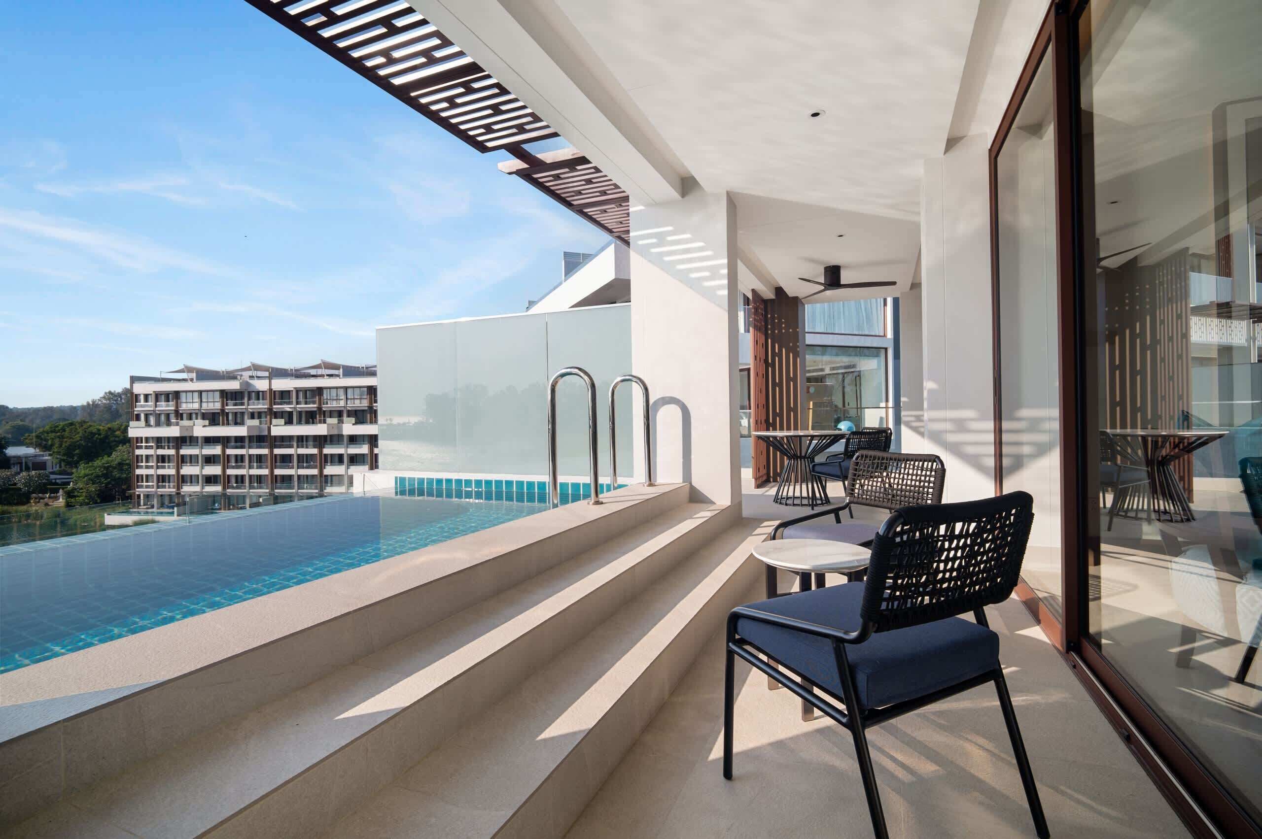Varanda moderna com guarda-corpo de vidro, com vista para uma piscina e um edifício ao fundo.