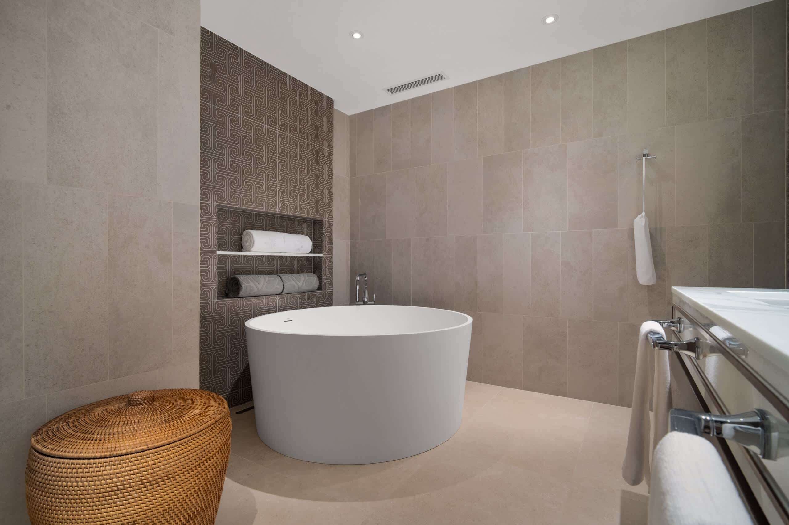 Un bagno moderno con una vasca freestanding, uno sgabello in vimini e un portasciugamani.
