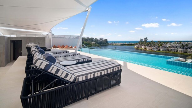 Ett modernt utomhusområde med loungekänsla, komplett med pool, solstolar och utsikt över havet.
