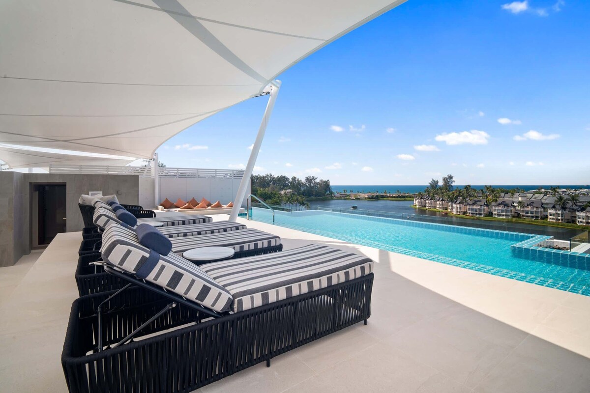 A modern outdoor lounge area with a pool, lounge chairs, and a view of the ocean.