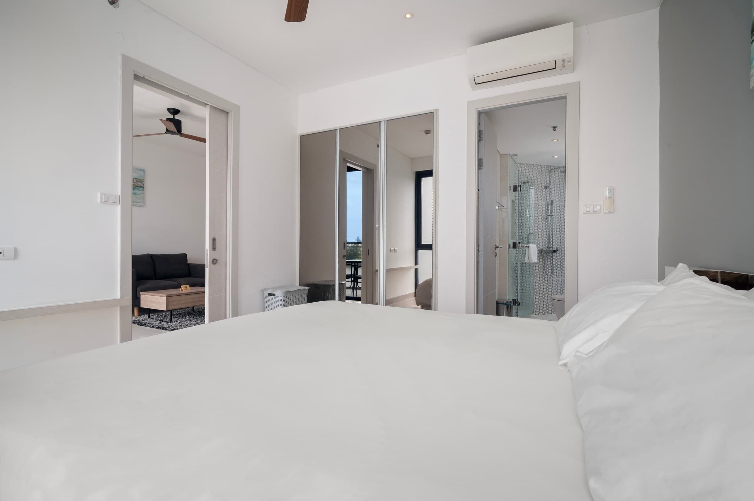 A modern hotel room with a large bed, a sofa, a small table, and a walk-in shower.