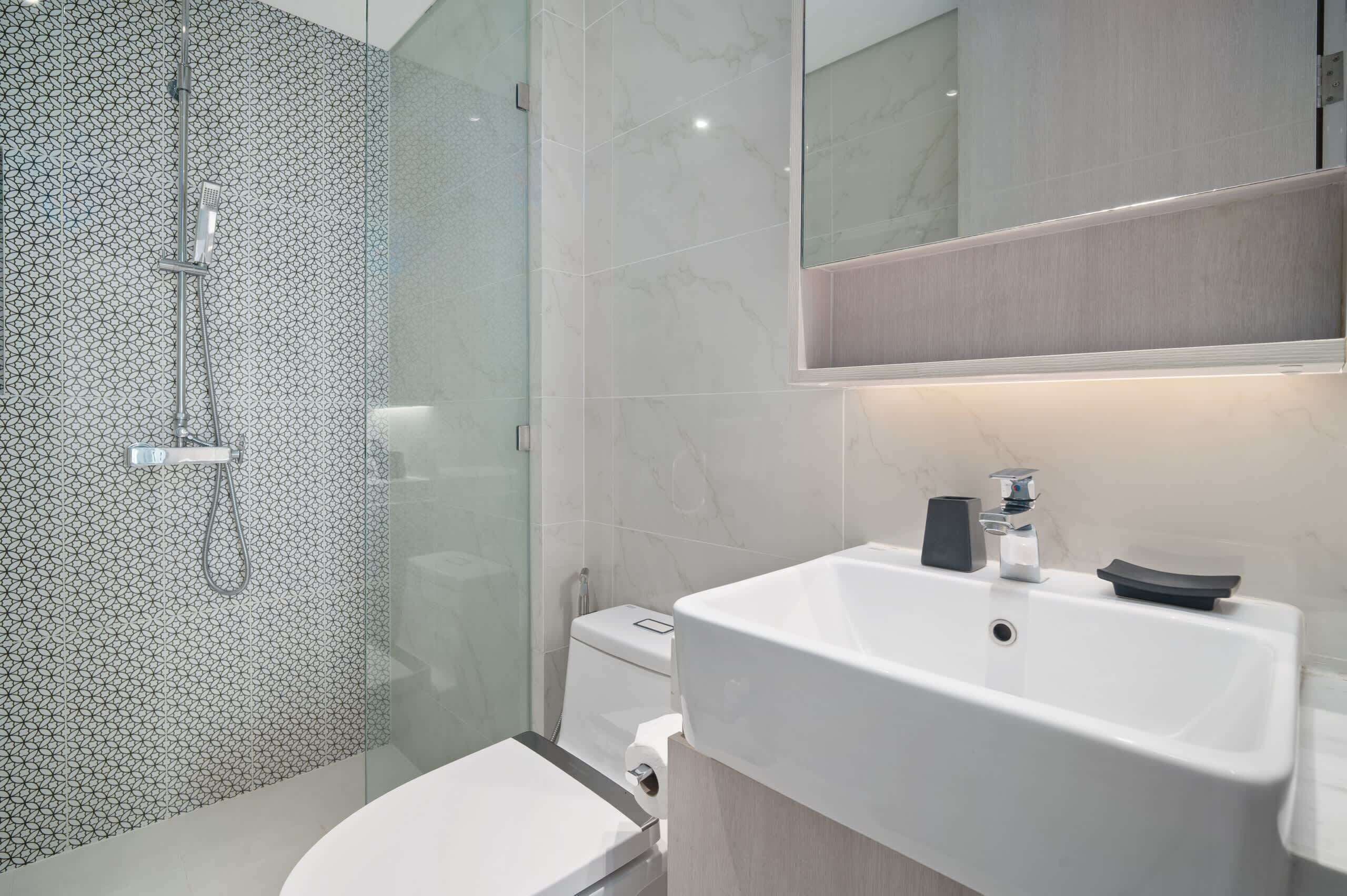 Un baño moderno con ducha envuelta en vidrio, inodoro blanco y lavabo blanco con un espejo encima.