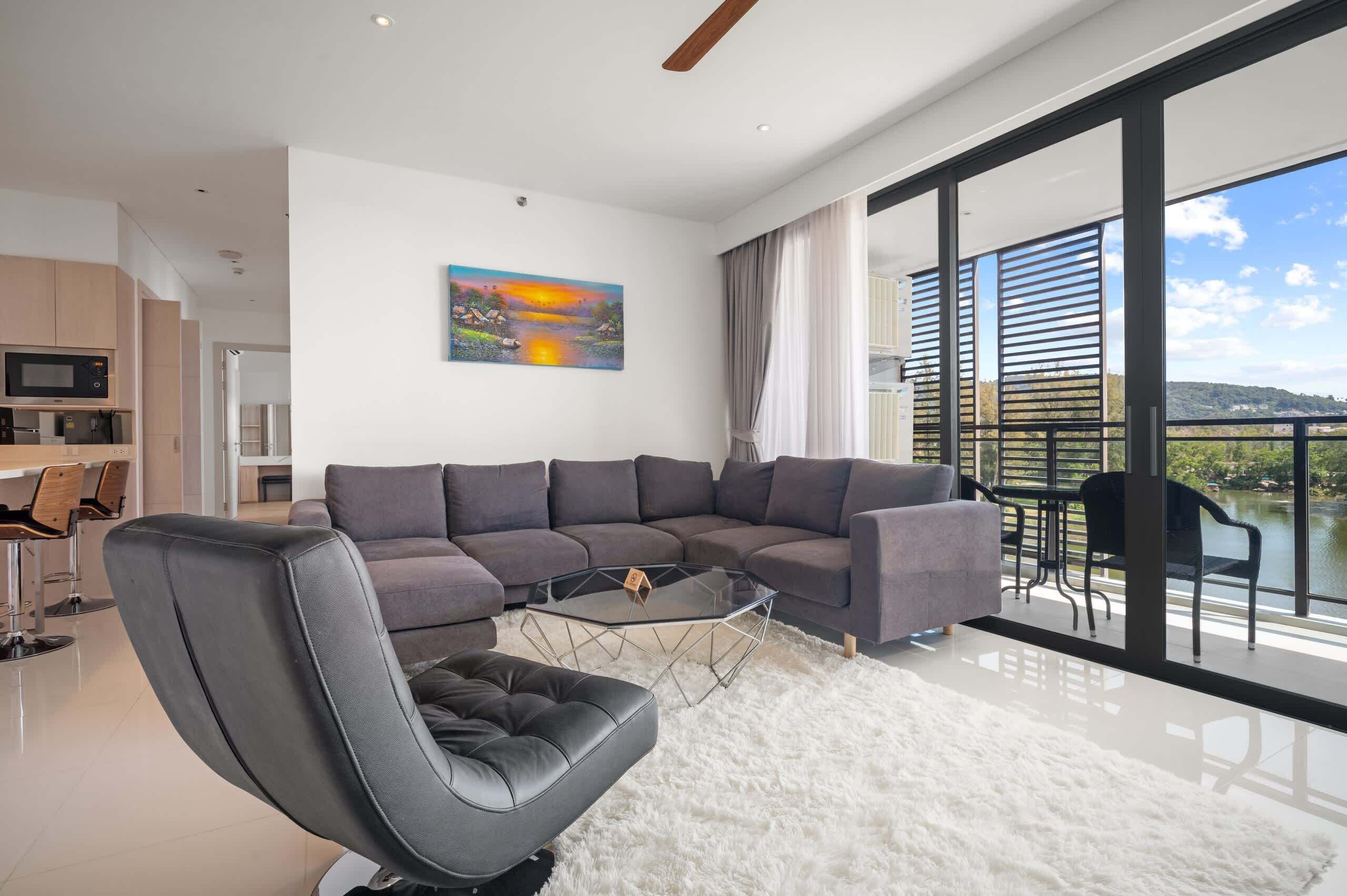 A modern living room with a sectional sofa, a glass coffee table, and a view of a lake through large windows.