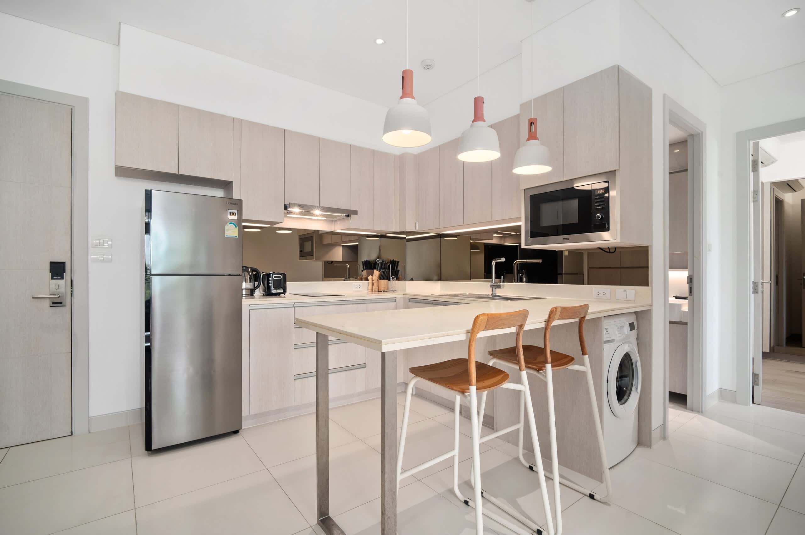 A modern kitchen with a stainless steel refrigerator, a microwave, a washing machine, and a bar stool.
