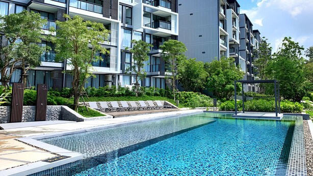 A modern building with balconies, a swimming pool, and surrounding greenery. - Cassia Residences Building 2 in Laguna by Banyan Living (Choeng Thale)