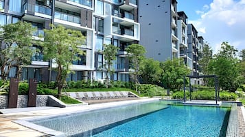 Un edificio moderno con balcones, piscina y follaje circundante.