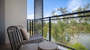 A balcony with a wicker chair and ottoman, overlooking a lake and trees. - Cassia Residences Building 2 in Laguna by Banyan Living (Choeng Thale)