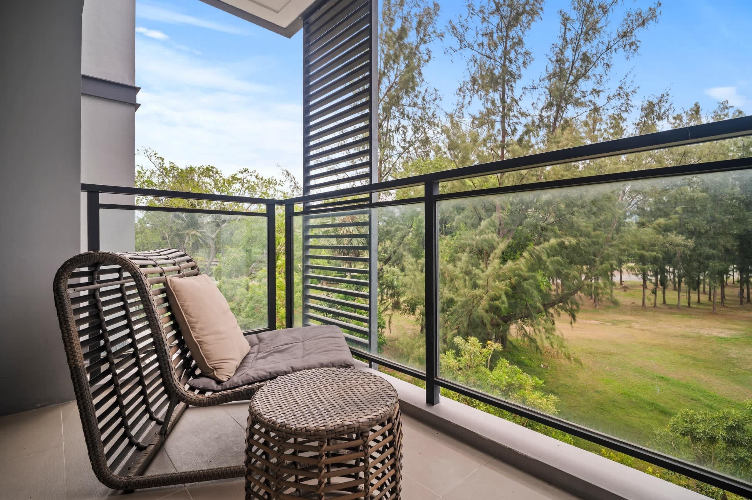 A balcony with a wicker chair and ottoman, large windows, and a view of a green landscape.