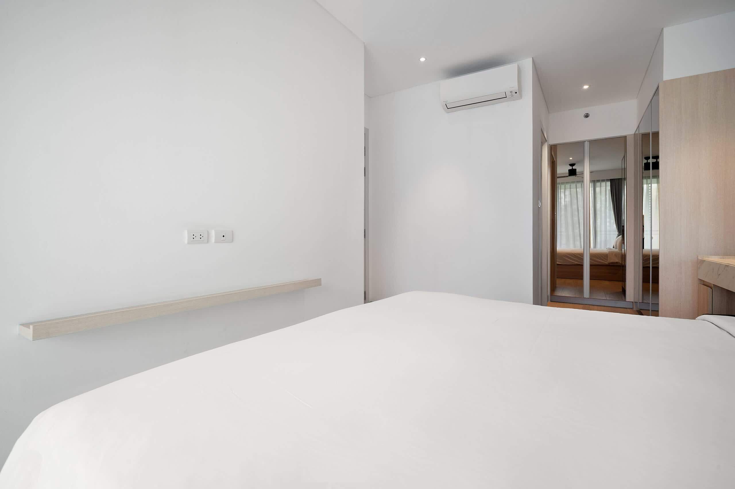 A modern hotel room with a large bed, a wooden bedside table, a built-in wardrobe, and a sliding glass door leading to a bathroom.