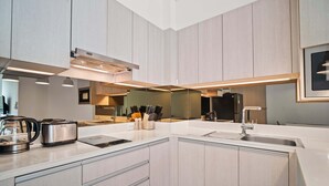 A modern kitchen with light wood cabinets, a white countertop, a built-in oven, and a coffee maker. - Cassia Residences Building 2 in Laguna by Banyan Living (Choeng Thale)