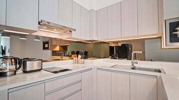 Una cocina moderna con armarios de madera clara, encimera blanca, horno empotrado y cafetera.