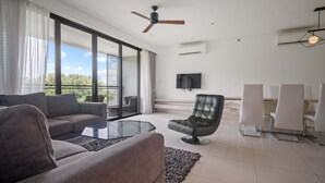A modern living room with a sofa, armchair, glass coffee table, and a TV mounted on the wall. - Cassia Residences Building 2 in Laguna by Banyan Living (Choeng Thale)